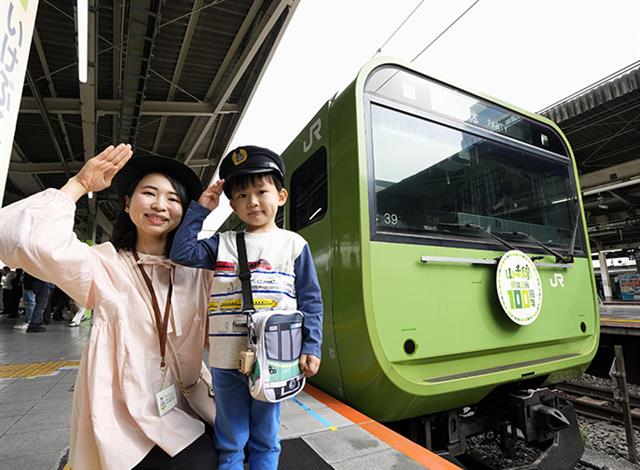 過去の車両デザインでラッピングした山手線の列車と写真におさまる親子=1日、JR池袋駅